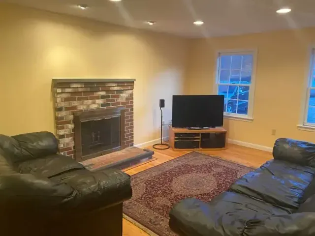 Living room with brick fireplace, leather sofas, TV, and patterned rug.