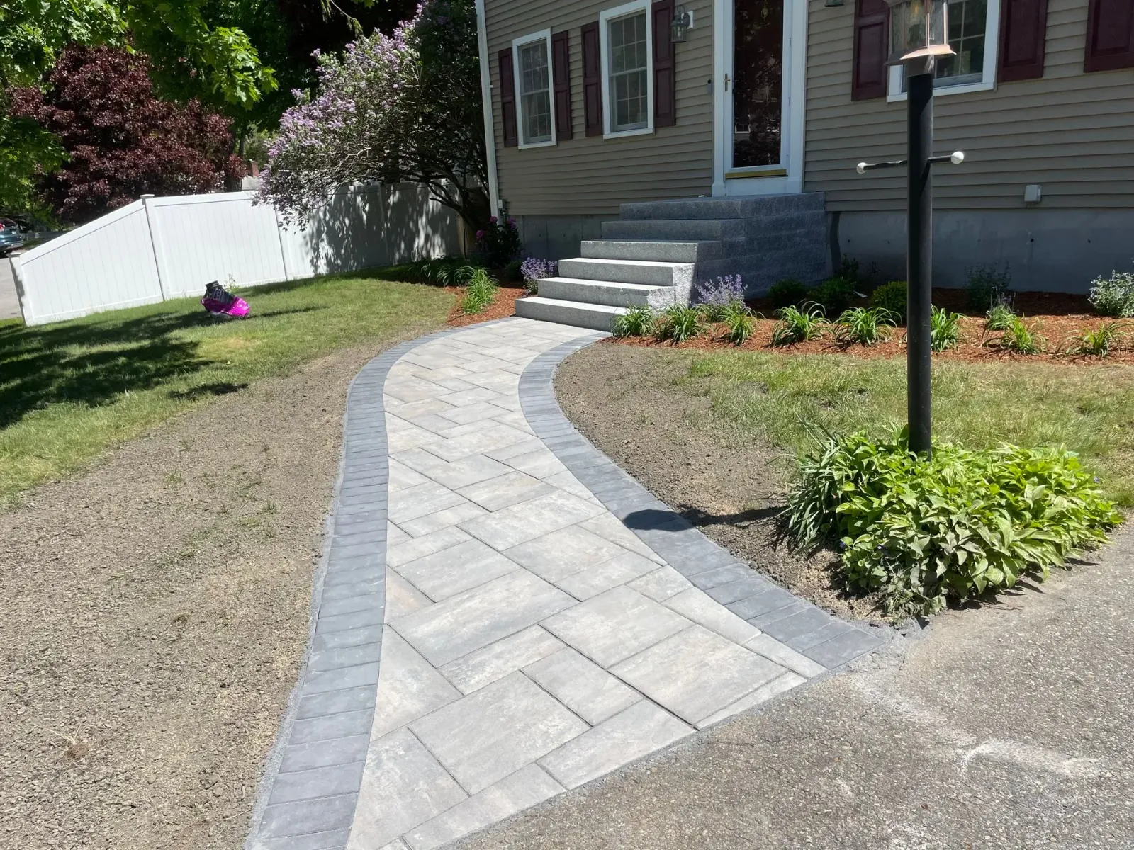 Curved stone walkway leading to a house entrance with steps, bordered by grass and flower beds
