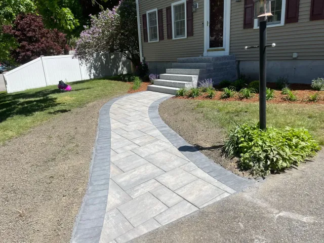 Curved stone walkway leading to a house entrance with steps, bordered by grass and flower beds