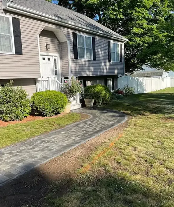 Curved dark paver front walkway leading from the lawn to the entrance of a raised home