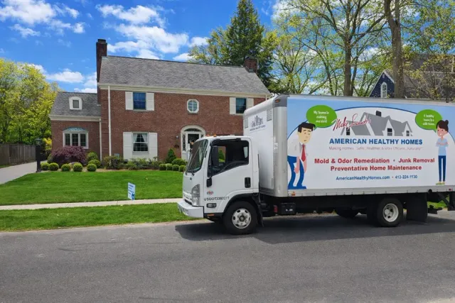 A Healthy Homes service truck parked on a residential street in front of a brick house.
