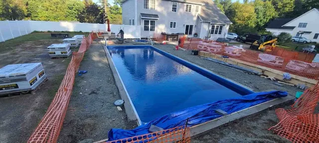 Backyard pool under construction with blue liner, orange safety fencing, and a house in the background