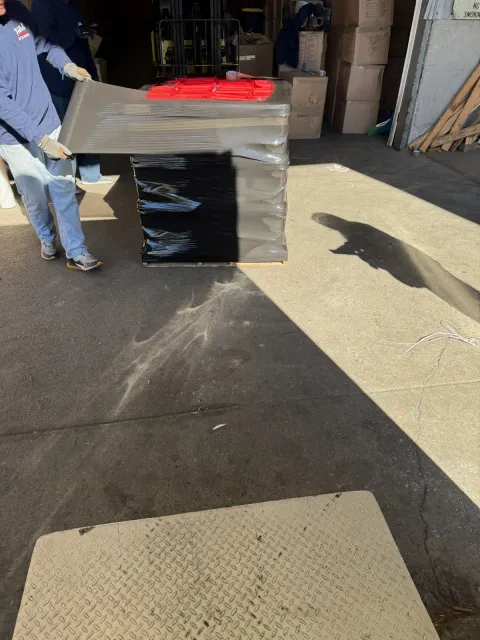 Crew member shrink-wrapping a pallet of boxed goods at a warehouse loading dock