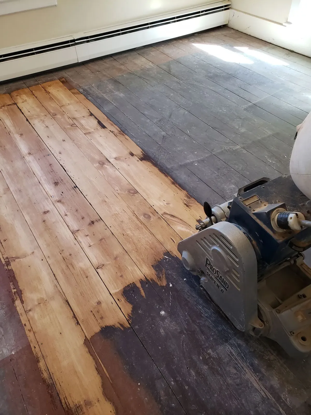 A person is sanding a wooden floor with a machine