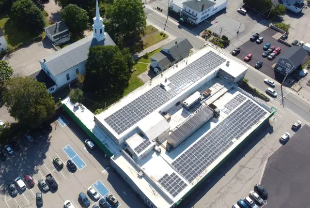 Aerial view of commercial building with solar panels and church in the background.