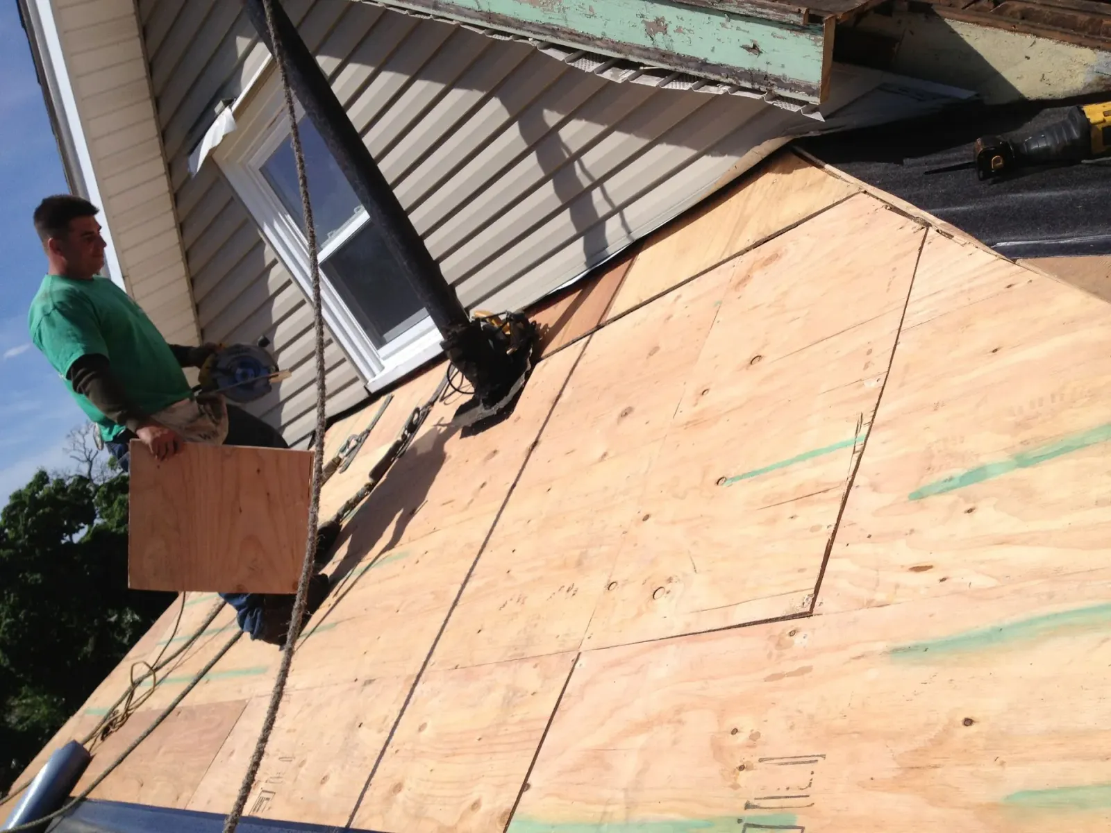 Workers roofing a house with plywood sheathing and ladder on the sloped roof