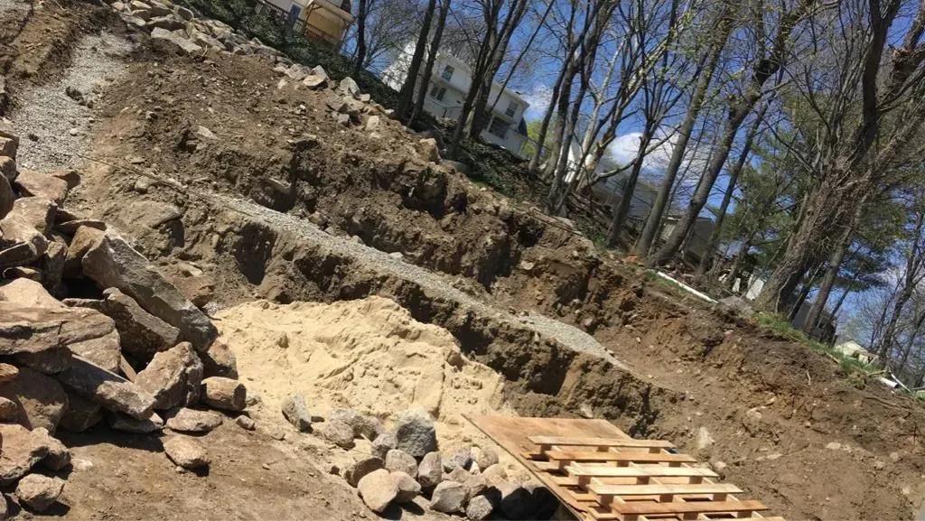 Rocky dirt slope at a construction site with stacked stones and a wooden pallet, under bare trees