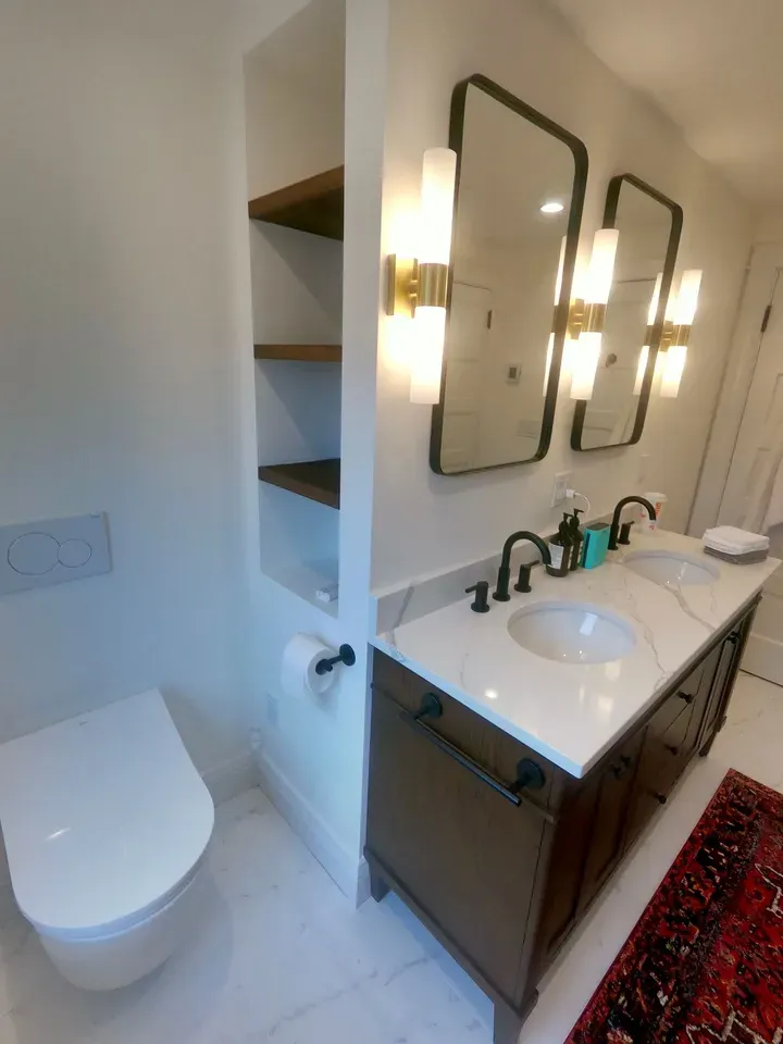 Bathroom with white walls, dual sinks, open shelving, and a toilet.