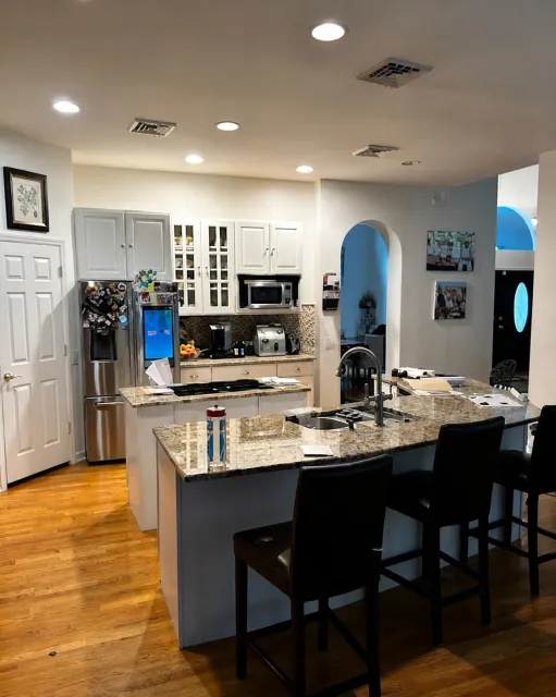 Bright modern kitchen with granite island, stainless appliances, bar stools, and hardwood floors