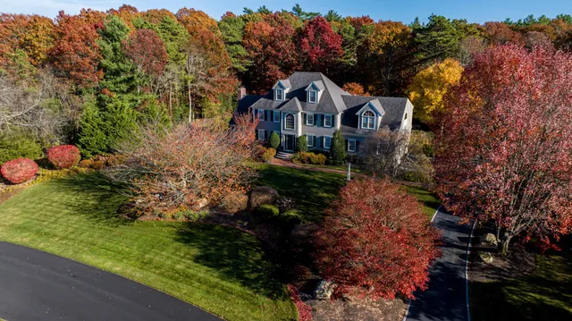 Aerial view of a large house surrounded by vibrant autumn trees, with a curved driveway and well-maintained lawn in a wooded setting.
