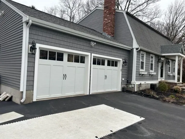 Gray house with white garage doors, black driveway, and dark shingles.