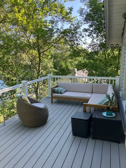 Outdoor deck with wicker furniture, including a round chair with cushions, a sectional sofa, and two ottomans, surrounded by trees in a natural setting.