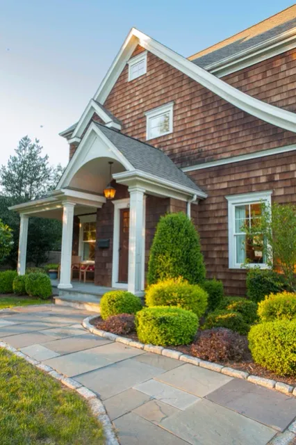A flagstone path leading to the front porch of a home with brown siding and well-maintained landscaping.