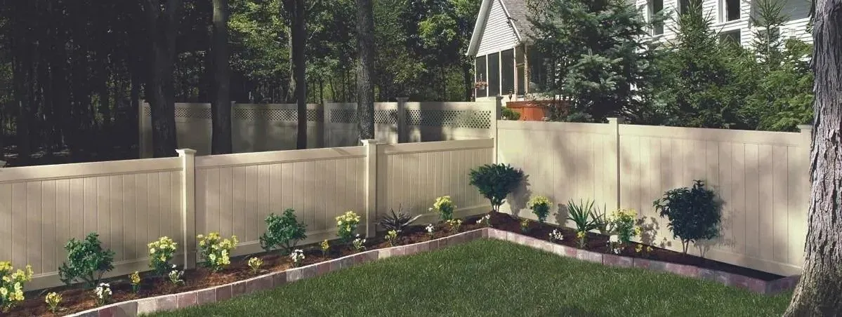 Landscaped backyard with a beige privacy fence, flower beds, and a small gazebo under trees.
