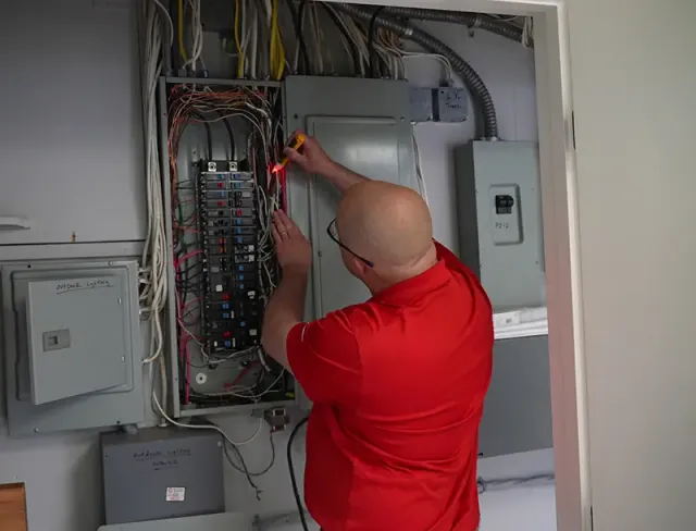 Electrician inspecting circuit breaker panel with multimeter, ensuring electrical safety and functionality for HVAC services in Taunton, MA.
