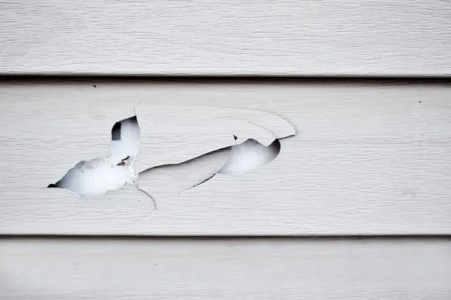 Torn white paint peeling off weathered wooden siding, showing damage and deterioration