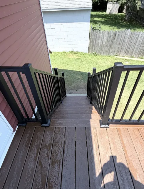 Wooden deck stairs with black railings leading down to a grassy backyard.