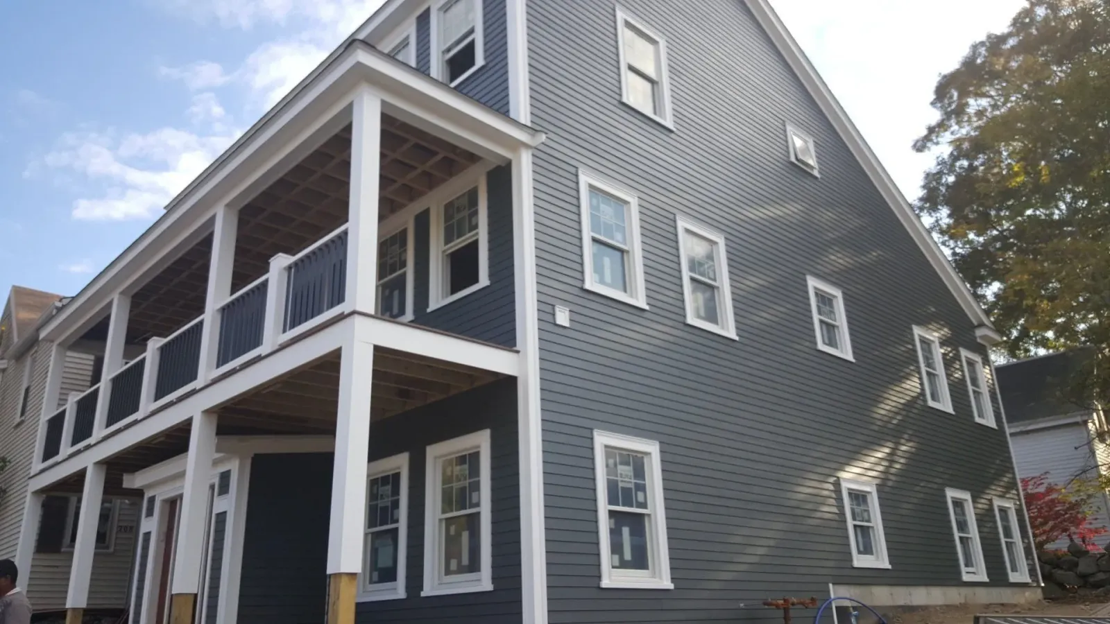 Gray two-story house with white trim and wraparound porch under a blue sky