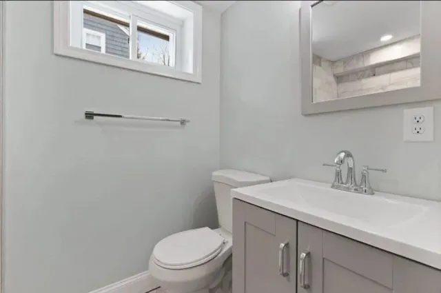 A bathroom with a toilet, sink, mirror and window.