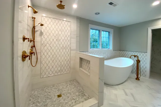 Custom bathroom tile design with gold fixtures, detailed mosaic tilework, and a freestanding bathtub.