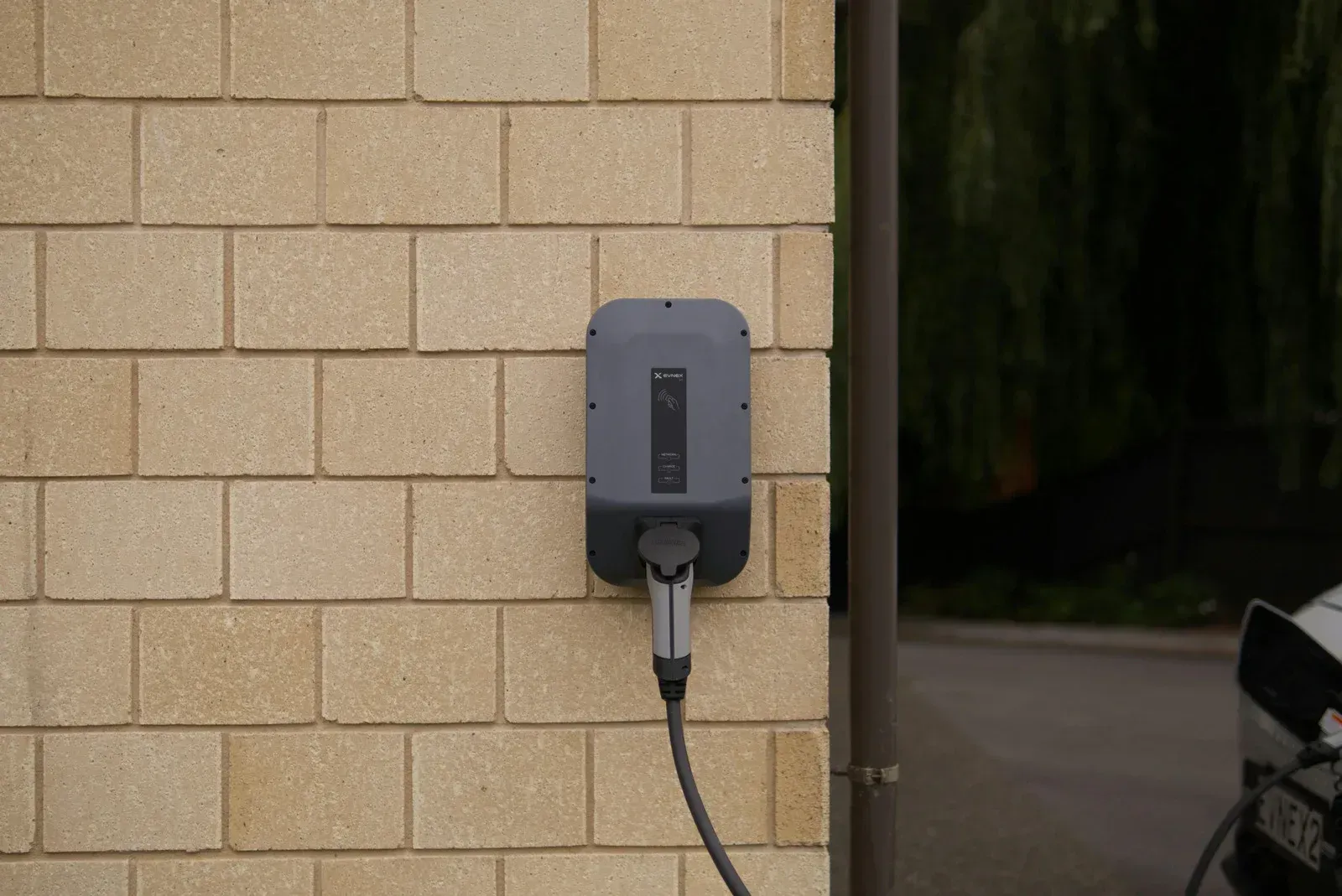 Electric vehicle charger mounted on a brick wall with a charging cable connected.
