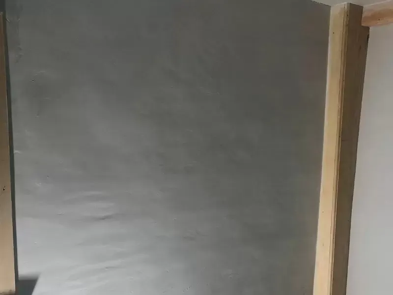 A smooth, gray plastered wall with wooden trim visible on the right side.