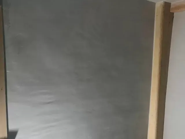 A smooth, gray plastered wall with wooden trim visible on the right side.