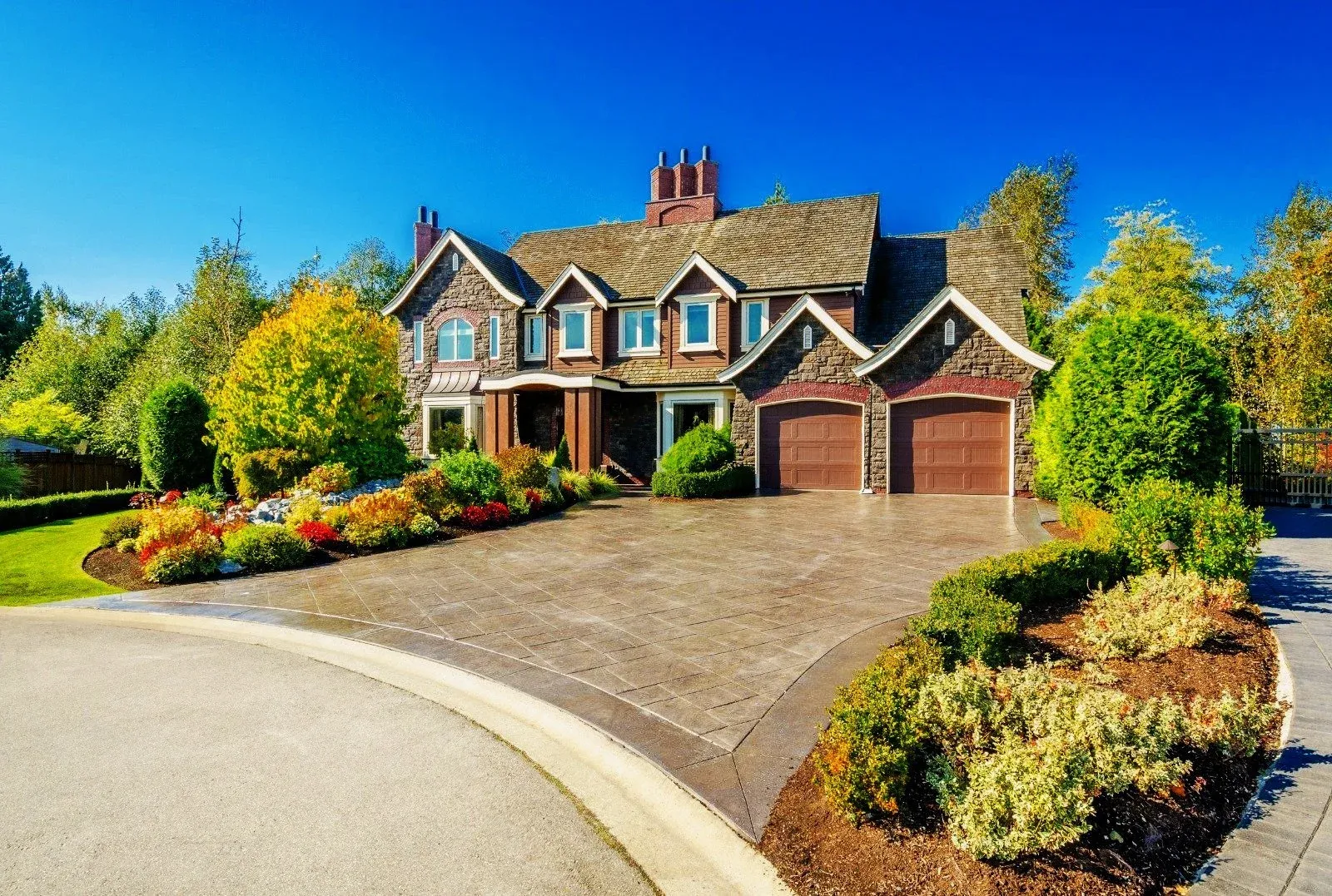 Custom stone masonry home with stamped concrete driveway, stone veneer façade, brick garage trim, and professional landscaping by expert masonry contractors in Massachusetts.