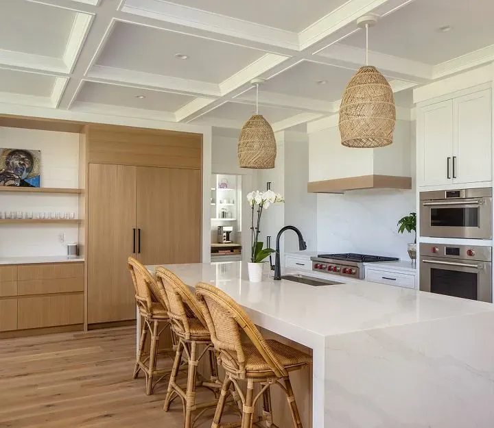 Bright modern kitchen with white island, wicker stools, wood accents, and woven pendant lights