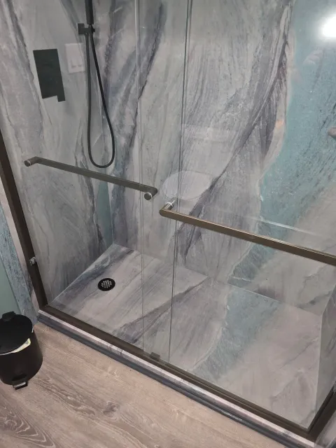 A shower stall with a marble wall and a glass door.