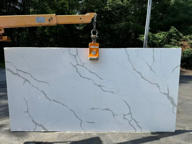 A large white granite slab is being lifted by a crane.