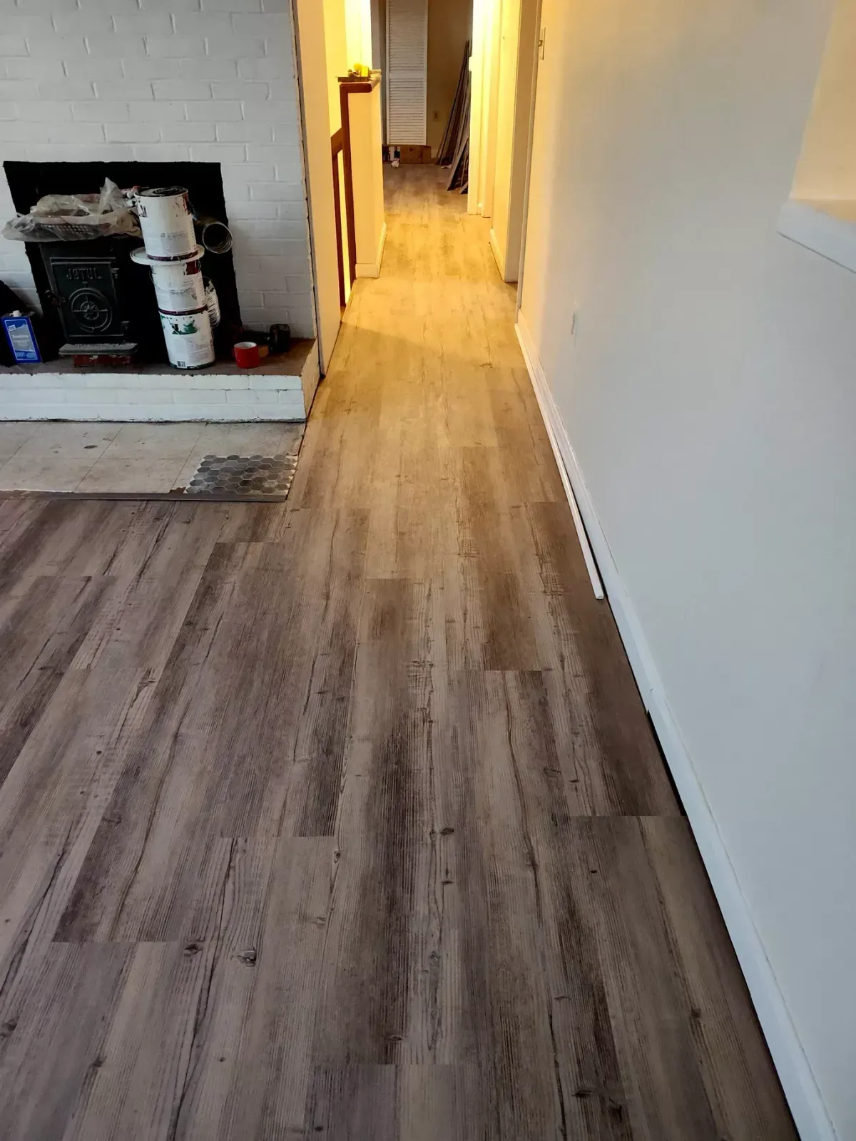 A view of wood-look vinyl plank flooring installed in a hallway leading toward a white brick fireplace.
