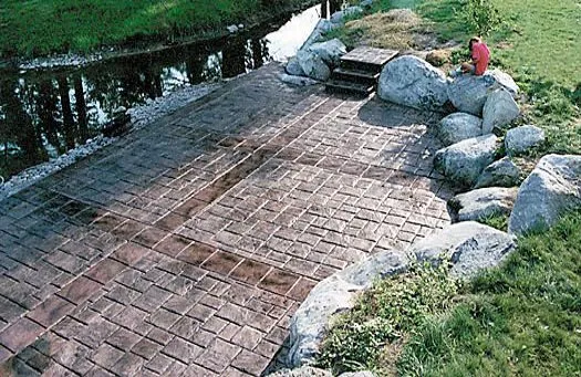 Brown stamped concrete patio with boulder accents by water