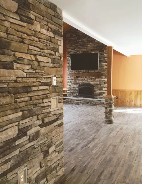 Living room with stone accent walls, a flat-screen TV mounted above a fireplace, and wood flooring.