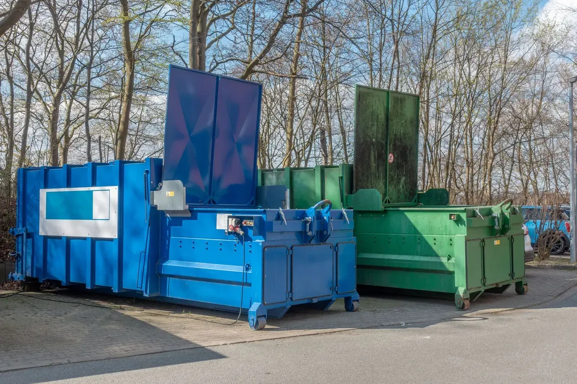 Blue and green industrial recycling containers outdoors by leafless trees