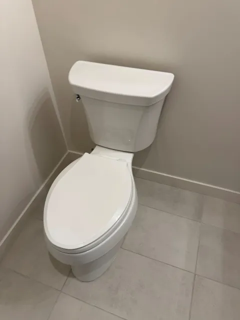 White toilet in a bathroom, against a beige wall, and white tiled floor.