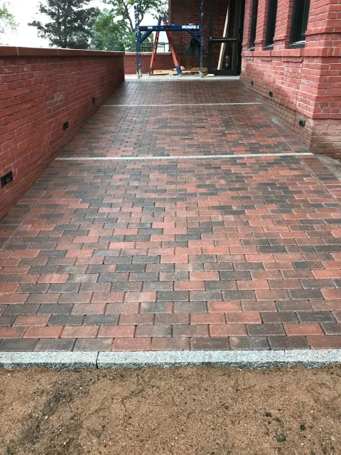 Brick walkway with red bricks and white accents, leading towards a building entrance.