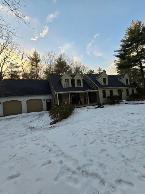 Snow-covered suburban house with a porch, garage, and footprints in the front yard at sunset.