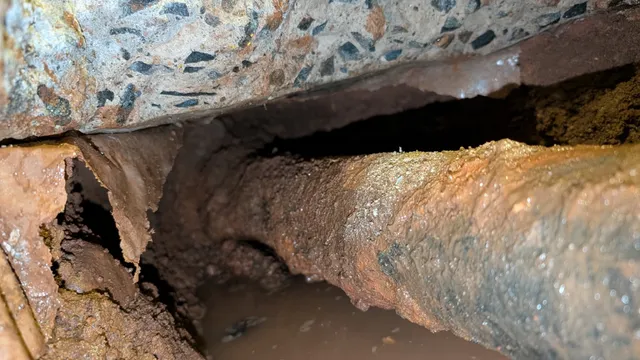 Close-up of the failure — the underside of the cast iron has rotted through, dumping waste and water directly into the soil beneath the slab.