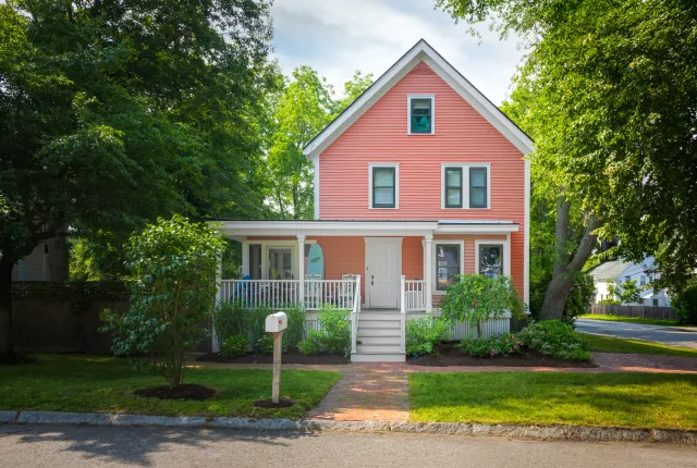 Front elevation with rose siding, white porch, dark windows, and central brick path
