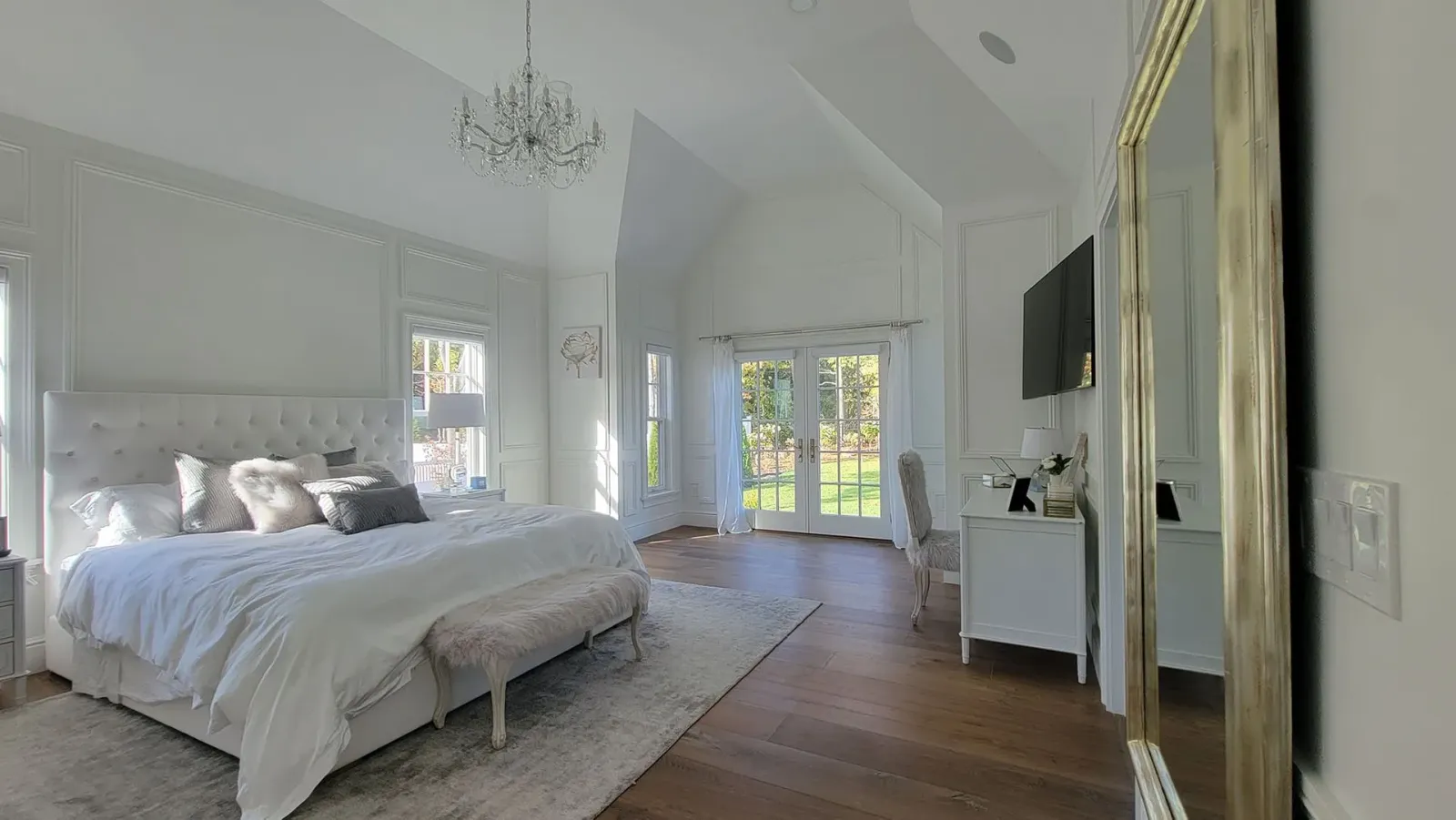 Bright white bedroom with a large bed, mirrored closet, and small desk by a window.