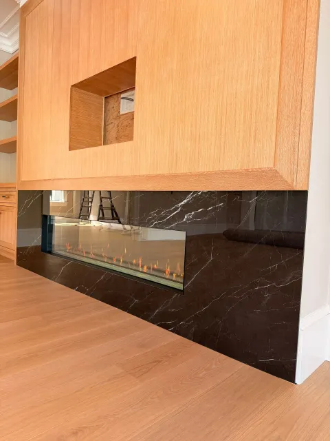 Wooden cabinet with a small rectangular cutout above a black marble fireplace opening