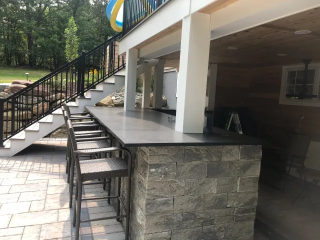 Outdoor patio area with a bar counter and four brown woven barstools, stone base