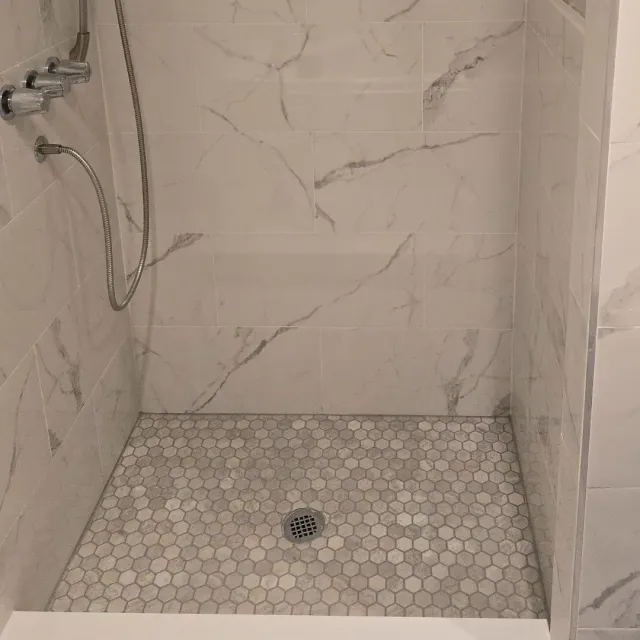 Marble-look porcelain shower with hexagon mosaic floor and built-in bench by Link Services Pro in Westborough, MA