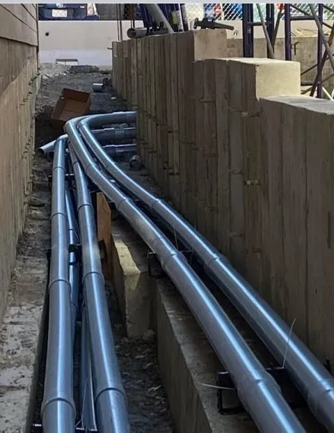 Construction site with multiple silver pipes running along the ground next to a wooden retaining wall.