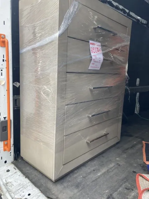 Wrapped chest of drawers inside a vehicle, ready for transport. The light-colored wood furniture has five drawers.