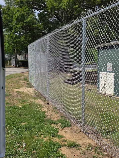 Chain-link fence beside a grassy path in a wooded outdoor area