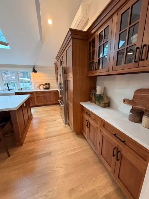 A kitchen with wooden cabinets, a marble countertop, and hardwood flooring. There is a window with a black faucet and a white island in the foreground.