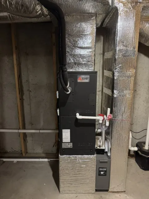 Furnace unit in a basement, with ductwork wrapped in silver insulation.