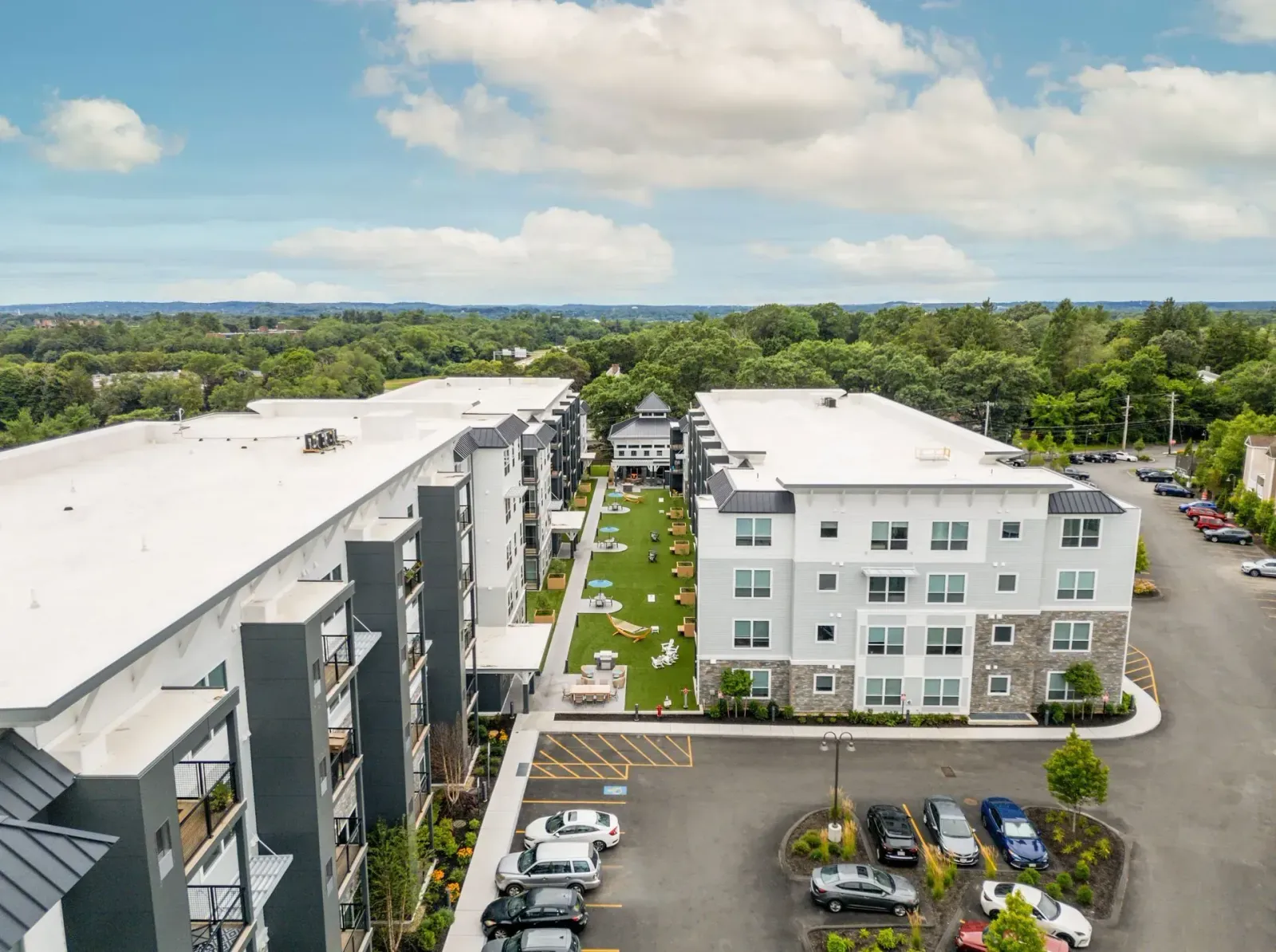 Aerial view of modern apartment complex with multiple buildings, a green courtyard, and parking lot.